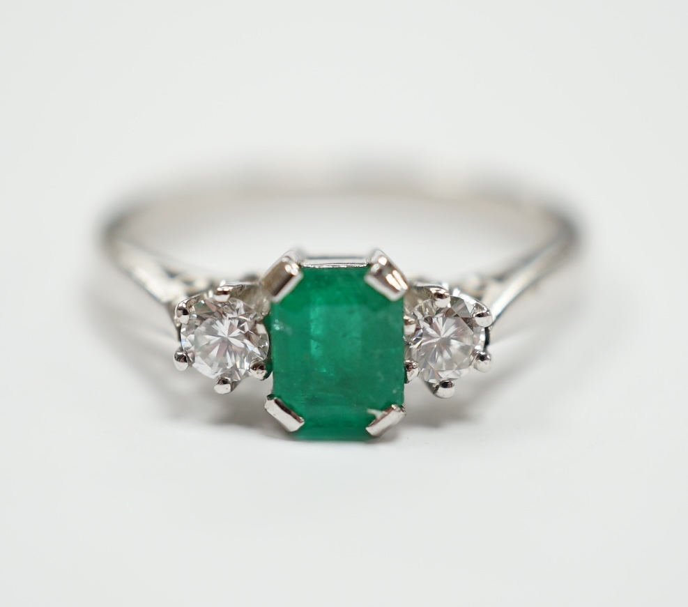 A modern 18ct white metal, single stone emerald and two stone diamond set ring, size N, gross weight 4 gram.